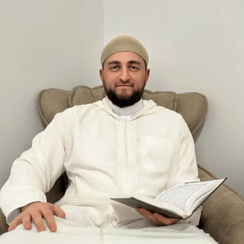 Cheikh Azamat, assis, un exemplaire du Coran ouvert à la main